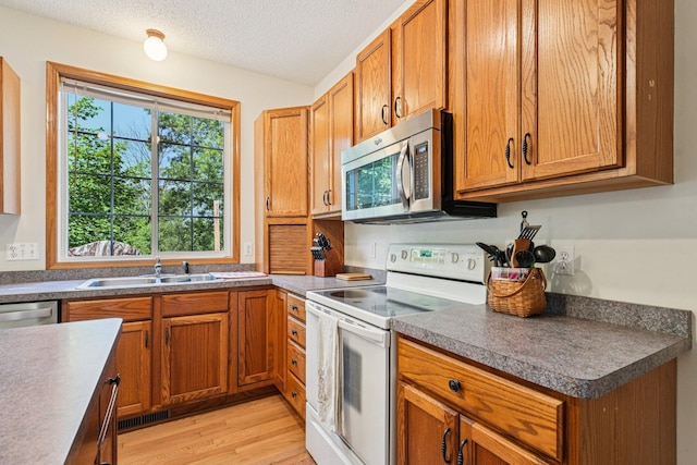 14916 Overlook Dr, Savage, MN 55378 - kitchen featuring appliances with stainless steel finishes, brown cabinets, light wood-type flooring, a textured ceiling, and dark countertops