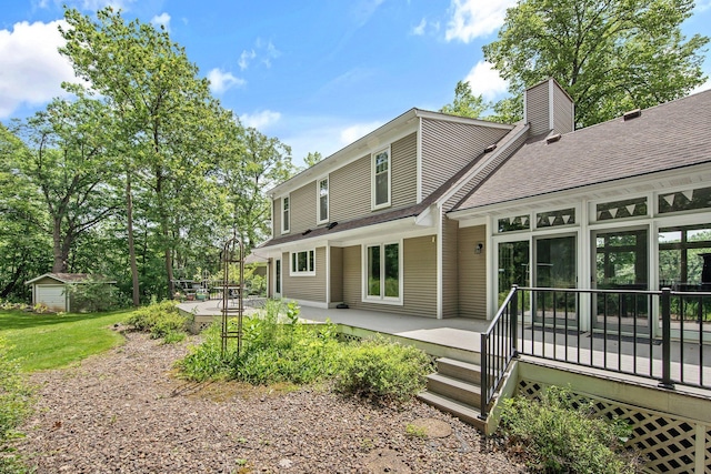 2261 Ash St, Lino Lakes, MN 55110 - back of property featuring a chimney, a deck, a shingled roof, a patio, and an outbuilding