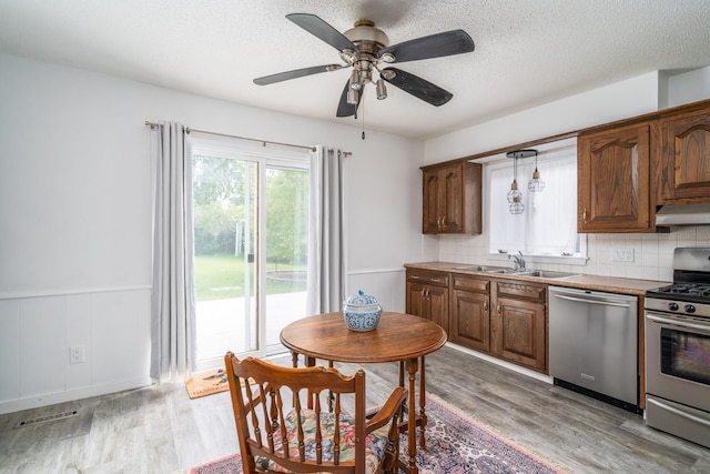 217 6th St, Crookston, MN 56716 - kitchen featuring stainless steel appliances, light wood-style floors, a wainscoted wall, under cabinet range hood, and backsplash