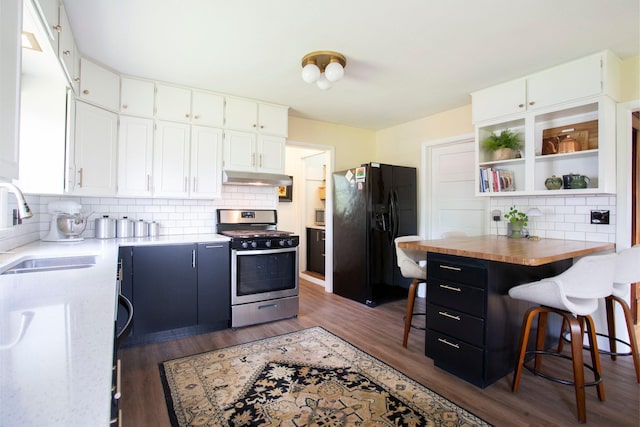 311 Fremont St, River Falls, WI 54022 - kitchen with gas stove, black refrigerator with ice dispenser, under cabinet range hood, tasteful backsplash, and white cabinetry