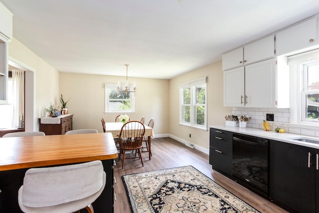 311 Fremont St, River Falls, WI 54022 - kitchen with black dishwasher, light countertops, light wood-type flooring, a chandelier, and white cabinets