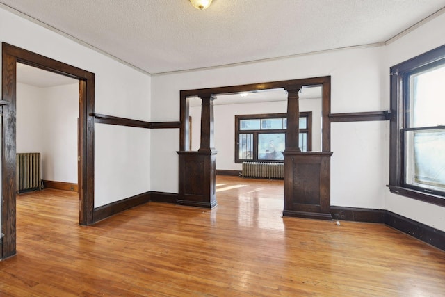 104 27th St, Minneapolis, MN 55408 - spare room with radiator heating unit, light wood-style flooring, ornate columns, and a textured ceiling