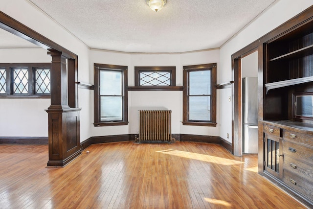 104 27th St, Minneapolis, MN 55408 - unfurnished living room featuring radiator heating unit, hardwood / wood-style floors, decorative columns, a textured ceiling, and healthy amount of natural light