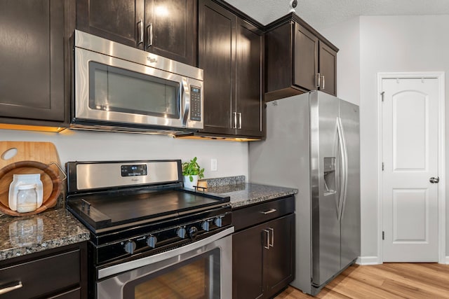 1174 139th St E, Rosemount, MN 55068 - kitchen featuring stainless steel appliances, light wood-style floors, dark stone countertops, dark brown cabinetry, and a textured ceiling
