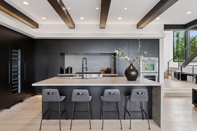 1300 Wildhurst Trl, Orono, MN 55364 - kitchen featuring modern cabinets, beam ceiling, light wood-style flooring, a kitchen bar, and light countertops