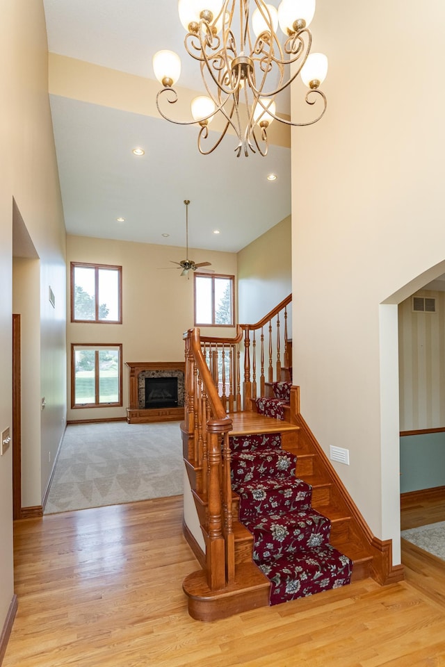 1608 Greystone Ln SW, Rochester, MN 55902 - staircase with a chandelier, wood finished floors, a fireplace with raised hearth, a ceiling fan, and a towering ceiling