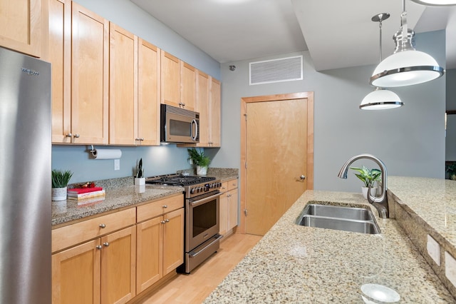 317 Groveland Ave Unit 106, Minneapolis, MN 55403 - kitchen featuring appliances with stainless steel finishes, light brown cabinets, light wood-type flooring, light stone countertops, and pendant lighting