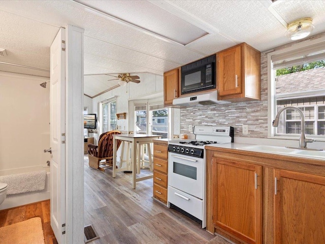 15827 Wilderness Trl Unit 30, Crosslake, MN 56442 - kitchen featuring white gas range oven, black microwave, under cabinet range hood, wood finished floors, and brown cabinetry
