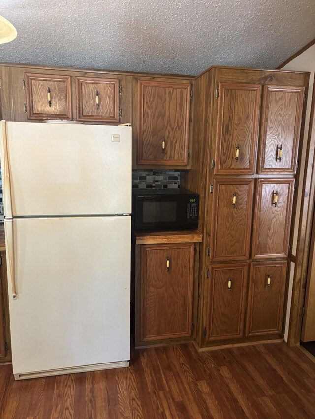 77165 Stepan Rd, Kettle River Twp, MN 55795 - kitchen featuring freestanding refrigerator, black microwave, brown cabinets, dark wood-type flooring, and a textured ceiling