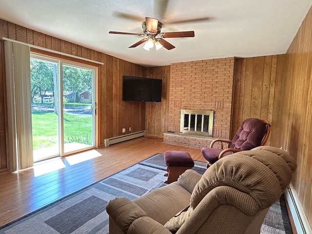 402 6th St NE, Barnesville, MN 56514 - living room with baseboard heating, wooden walls, wood finished floors, a ceiling fan, and a brick fireplace