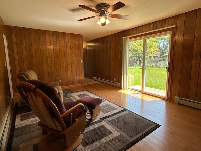 402 6th St NE, Barnesville, MN 56514 - living area with a baseboard heating unit, wooden walls, a ceiling fan, and hardwood / wood-style flooring