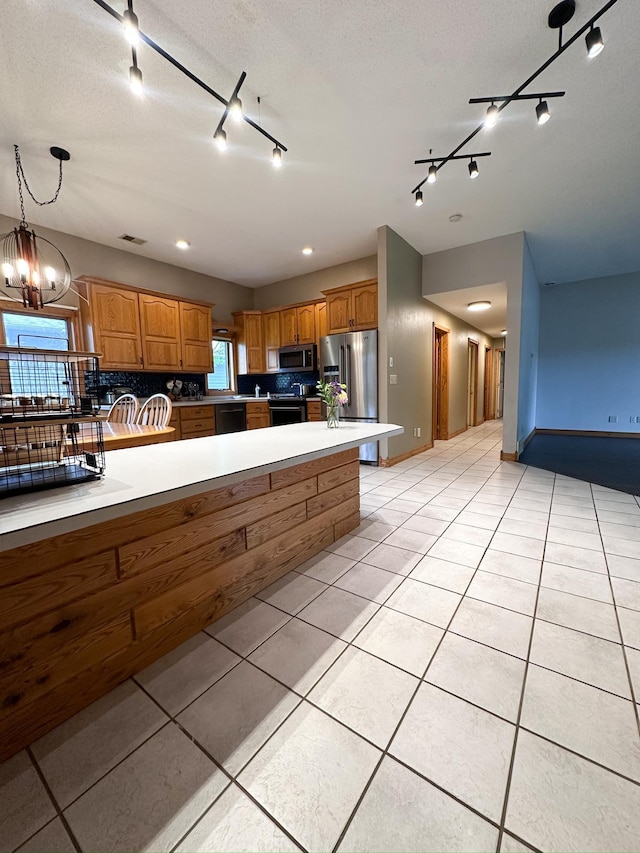 405 Fir Ave, Frazee, MN 56544 - kitchen featuring rail lighting, stainless steel appliances, brown cabinets, light tile patterned floors, and backsplash