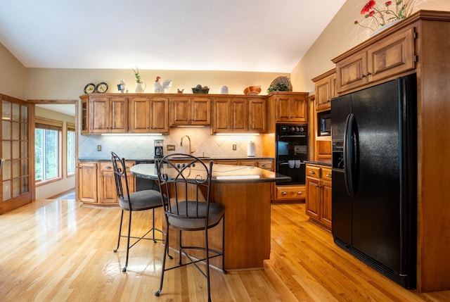 8980 160th Ln NW, Ramsey, MN 55303 - kitchen featuring black appliances, brown cabinetry, a kitchen bar, a center island with sink, and light wood-style flooring