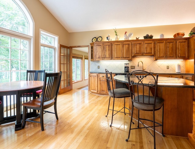 8980 160th Ln NW, Ramsey, MN 55303 - kitchen featuring lofted ceiling, brown cabinetry, light wood-type flooring, a breakfast bar area, and decorative backsplash