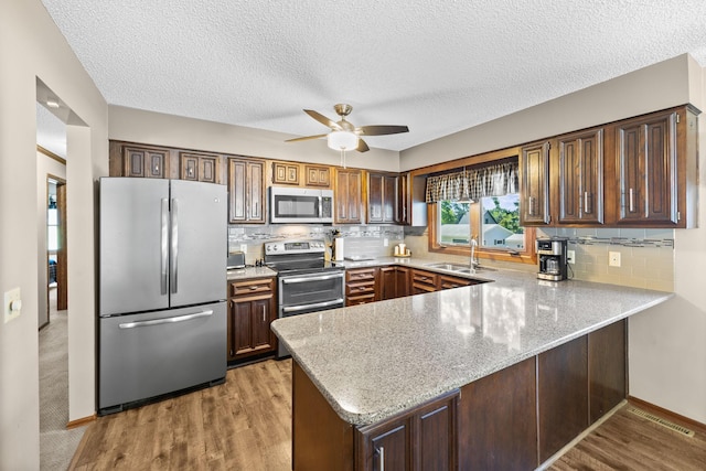 70190 218th St, Dassel, MN 55325 - kitchen with appliances with stainless steel finishes, a peninsula, light stone counters, ceiling fan, and backsplash