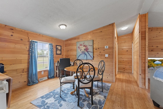713 Center St, Chetek, WI 54728 - dining area featuring wood walls, light wood-type flooring, vaulted ceiling, and a textured ceiling