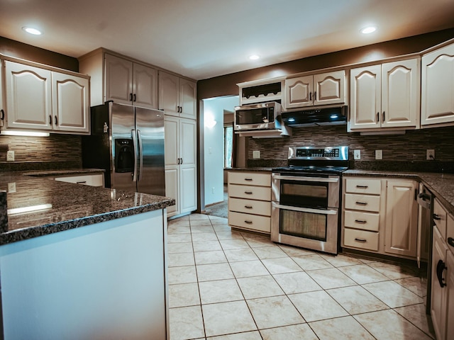 610 25th St SW, Austin, MN 55912 - kitchen featuring stainless steel appliances, under cabinet range hood, decorative backsplash, light tile patterned floors, and dark stone countertops