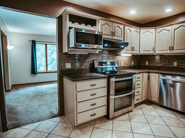 610 25th St SW, Austin, MN 55912 - kitchen featuring appliances with stainless steel finishes, light tile patterned flooring, light colored carpet, dark countertops, and backsplash
