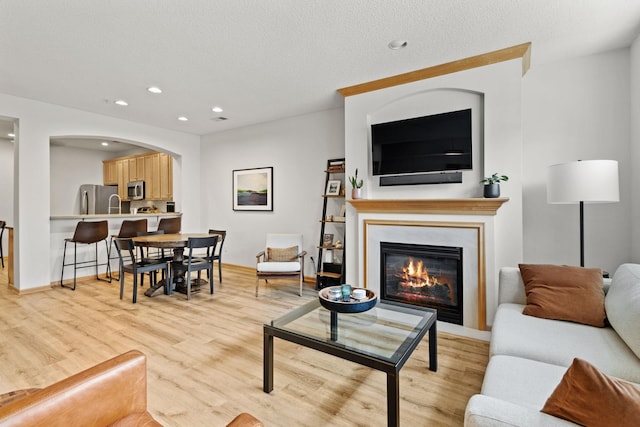 8479 Forestview Ln N, Maple Grove, MN 55369 - living room featuring light wood-style flooring, recessed lighting, a glass covered fireplace, and arched walkways