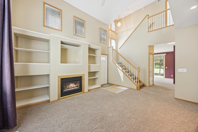 14000 Erwin Ct, Eden Prairie, MN 55344 - unfurnished living room featuring carpet, a glass covered fireplace, built in shelves, stairs, and a towering ceiling