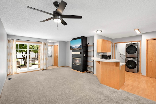 1830 Donegal Dr Unit 11, Woodbury, MN 55125 - kitchen featuring stacked washer / drying machine, a glass covered fireplace, a textured ceiling, a peninsula, and light brown cabinets