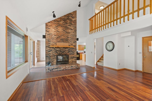 20170 Oxboro Ln N, Scandia, MN 55047 - unfurnished living room with wood-type flooring, stairs, high vaulted ceiling, and a brick fireplace