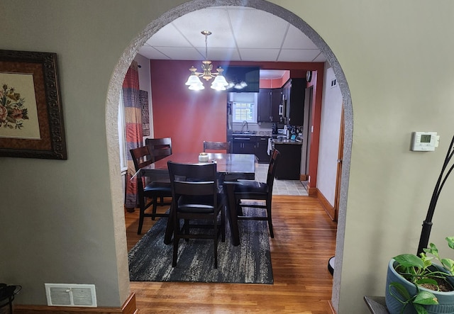 717 2nd Ave SW, Pipestone, MN 56164 - dining room featuring arched walkways, light wood finished floors, a chandelier, and a paneled ceiling