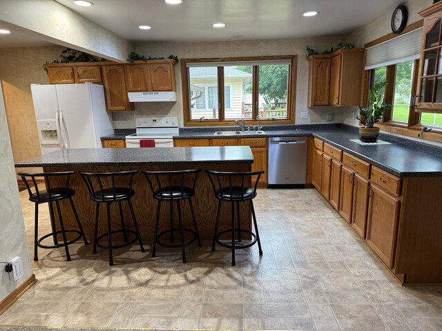 1204 Garflield Ave, Albert Lea, MN 56007 - kitchen with white appliances, under cabinet range hood, brown cabinetry, a kitchen island, and recessed lighting
