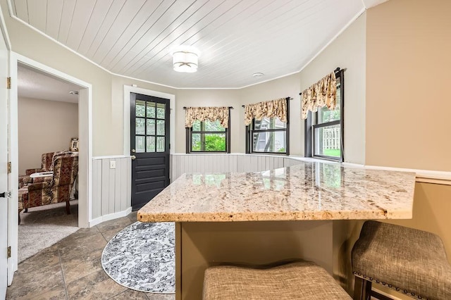 791 139th Ln NW, Andover, MN 55304 - kitchen featuring wainscoting, crown molding, light stone counters, stone finish floors, and a kitchen bar