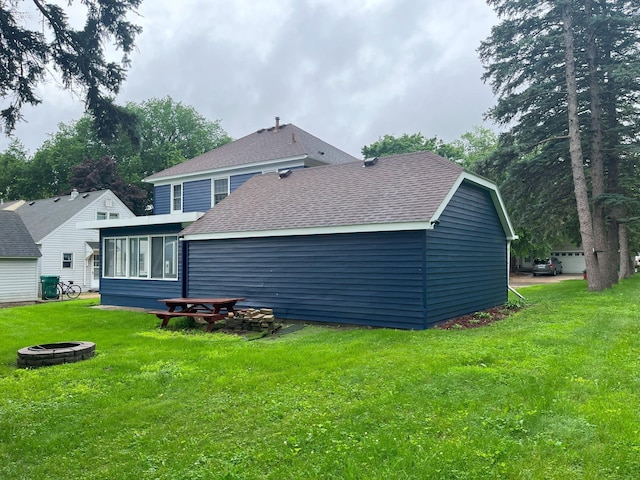 1304 3rd St NW, Austin, MN 55912 - rear view of house featuring a fire pit, a shingled roof, a yard, and a sunroom