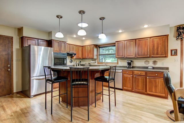 715 River Heights Rd SW, Menomonie, WI 54751 - kitchen featuring stainless steel appliances, light wood finished floors, dark countertops, brown cabinets, and under cabinet range hood