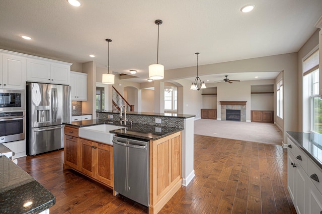 6430 Bluestem Cir, Corcoran, MN 55340 - kitchen featuring appliances with stainless steel finishes, a ceiling fan, arched walkways, dark wood-type flooring, and a tile fireplace