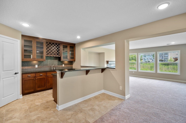 6430 Bluestem Cir, Corcoran, MN 55340 - kitchen with a kitchen bar, glass insert cabinets, brown cabinets, light colored carpet, and decorative backsplash