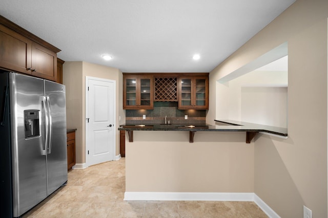 6430 Bluestem Cir, Corcoran, MN 55340 - kitchen featuring stainless steel fridge with ice dispenser, a kitchen bar, glass insert cabinets, dark stone counters, and backsplash