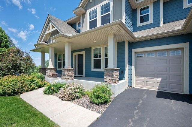 6430 Bluestem Cir, Corcoran, MN 55340 - doorway to property featuring covered porch, a shingled roof, an attached garage, stone siding, and asphalt driveway
