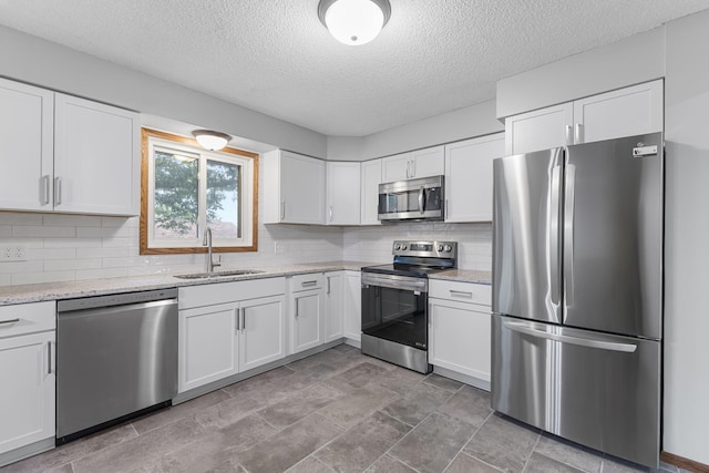 11460 Goldenrod St NW, Coon Rapids, MN 55448 - kitchen featuring stainless steel appliances, a textured ceiling, white cabinets, tasteful backsplash, and light stone counters