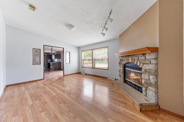 108 Hilton Ct, Mankato, MN 56001 - unfurnished living room with light wood finished floors, a fireplace, a textured ceiling, lofted ceiling, and rail lighting