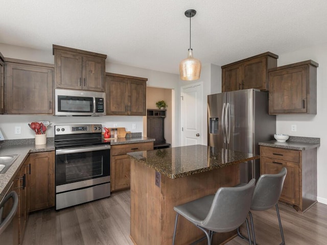 910 Burton Cir, Montrose, MN 55363 - kitchen with appliances with stainless steel finishes, dark wood finished floors, a center island, dark stone countertops, and a textured ceiling