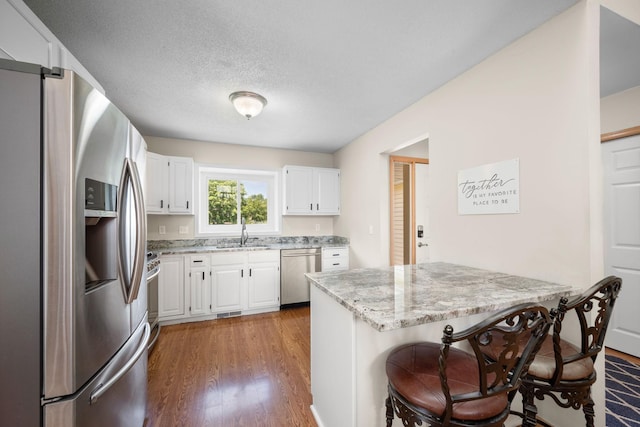 16391 Adret Ct, Eden Prairie, MN 55346 - kitchen featuring stainless steel appliances, light stone counters, light wood-type flooring, white cabinets, and a kitchen bar