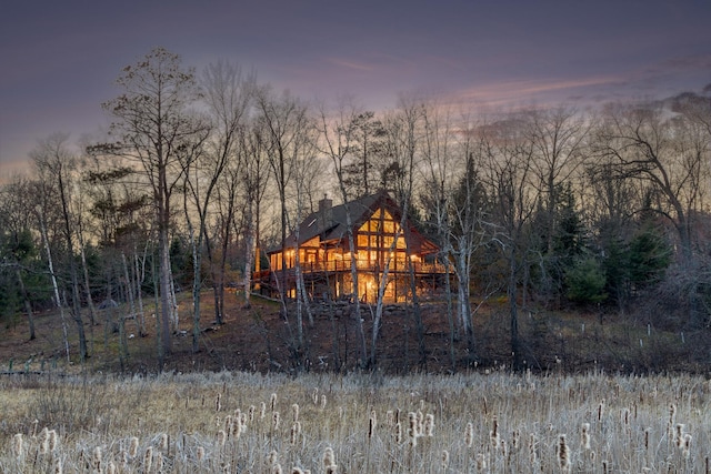15193 Wilderness Trl, Crosslake, MN 56442 - back of property at dusk featuring a chimney, a view of trees, and a wooden deck