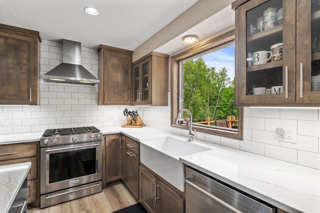 9950 204th Street Ct N, Forest Lake, MN 55025 - kitchen featuring appliances with stainless steel finishes, wall chimney range hood, light stone counters, light wood-style flooring, and backsplash