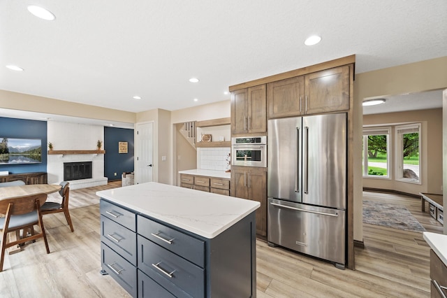 9950 204th Street Ct N, Forest Lake, MN 55025 - kitchen featuring appliances with stainless steel finishes, light wood-type flooring, a kitchen island, a brick fireplace, and open shelves