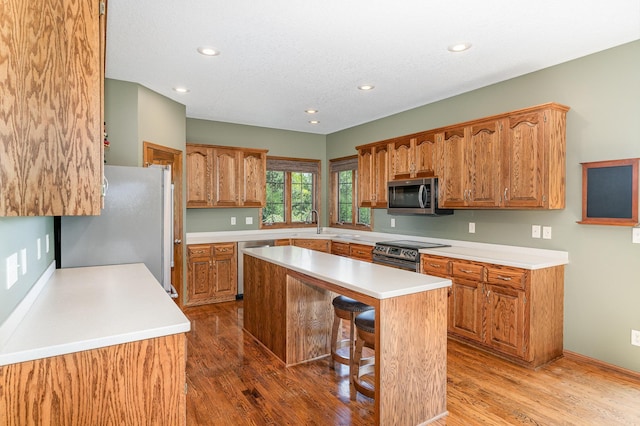 517 Redpoll Ave SE, New Prague, MN 56071 - kitchen featuring appliances with stainless steel finishes, a kitchen island, brown cabinetry, wood finished floors, and recessed lighting