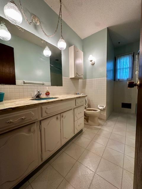 2671 4th Ave NE, Rochester, MN 55906 - bathroom featuring tile walls, vanity, a textured ceiling, a wainscoted wall, and tile patterned flooring