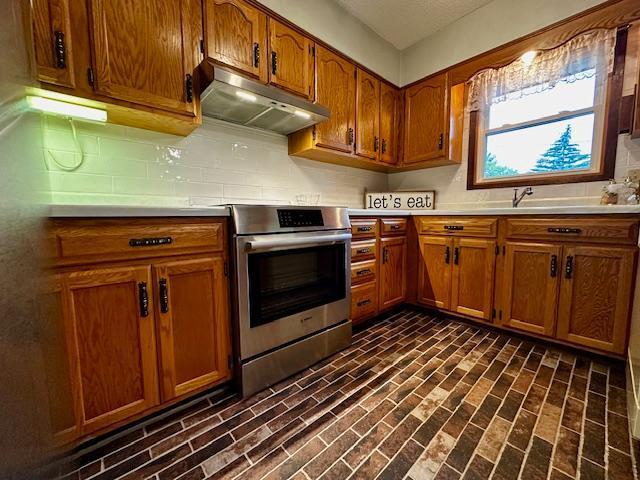 2671 4th Ave NE, Rochester, MN 55906 - kitchen with stainless steel electric stove, under cabinet range hood, brown cabinets, light countertops, and decorative backsplash