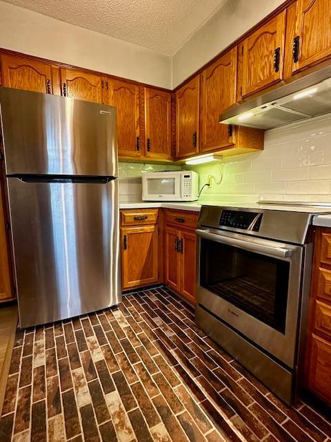 2671 4th Ave NE, Rochester, MN 55906 - kitchen with appliances with stainless steel finishes, under cabinet range hood, brown cabinetry, backsplash, and a textured ceiling