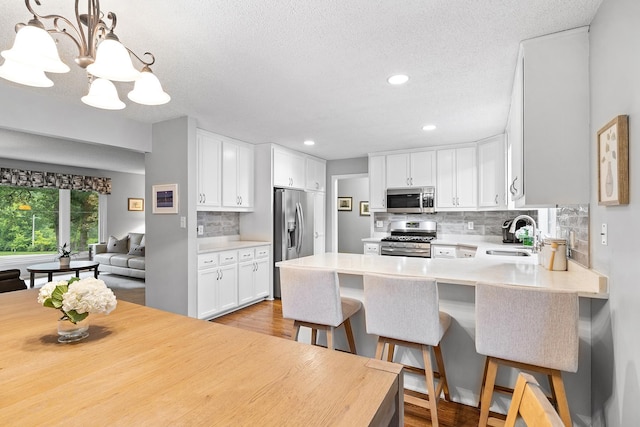 6721 Limerick Ln, Edina, MN 55439 - kitchen with stainless steel appliances, a chandelier, light wood-type flooring, a peninsula, and decorative backsplash