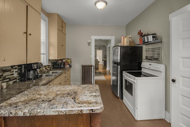310 4th Ave SW, Hutchinson, MN 55350 - kitchen with white electric stove, decorative backsplash, radiator, light wood-type flooring, and freestanding refrigerator