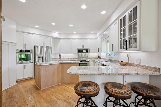5625 Zachary Ln N, Plymouth, MN 55442 - kitchen featuring appliances with stainless steel finishes, light stone countertops, light wood-type flooring, glass insert cabinets, and a breakfast bar