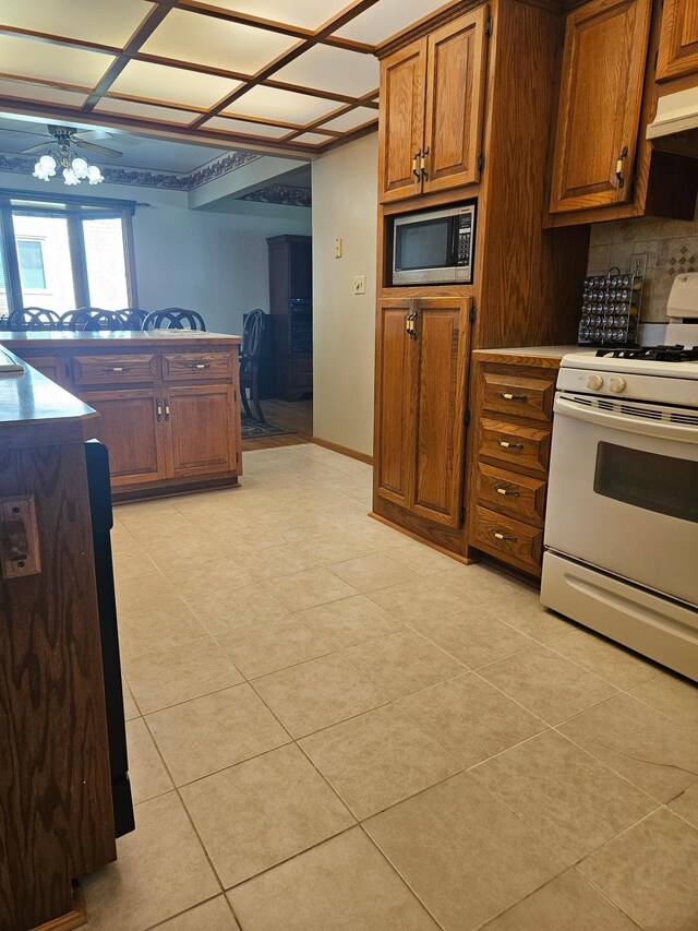 5306 Boulder Ln, Brooklyn Center, MN 55429 - kitchen featuring white range with gas cooktop, stainless steel microwave, light tile patterned floors, brown cabinetry, and custom exhaust hood